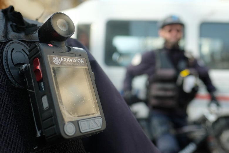 A police officer stands guard with a body camera attached to the shoulder.